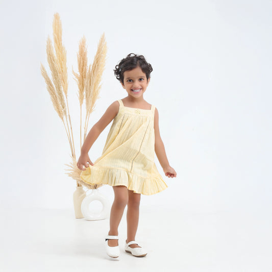 Young girl in a yellow dress standing next to dried pampas grass on a white background