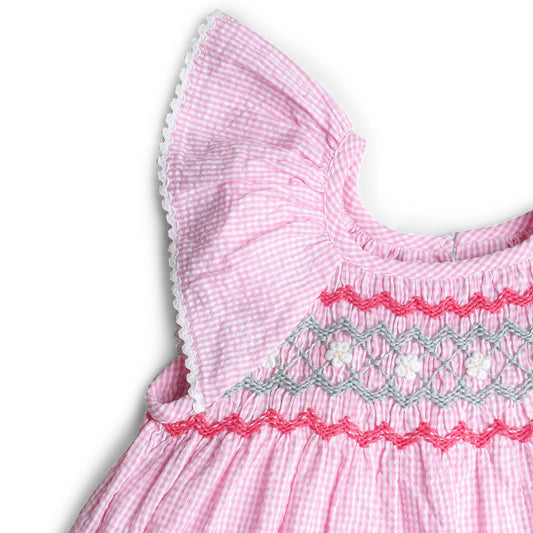 Close-up of a pink dress with smocked details on a white background